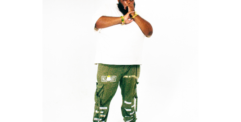 Full-length portrait of a man in a white t-shirt, olive green pants, and a red cap, posed against a white background.