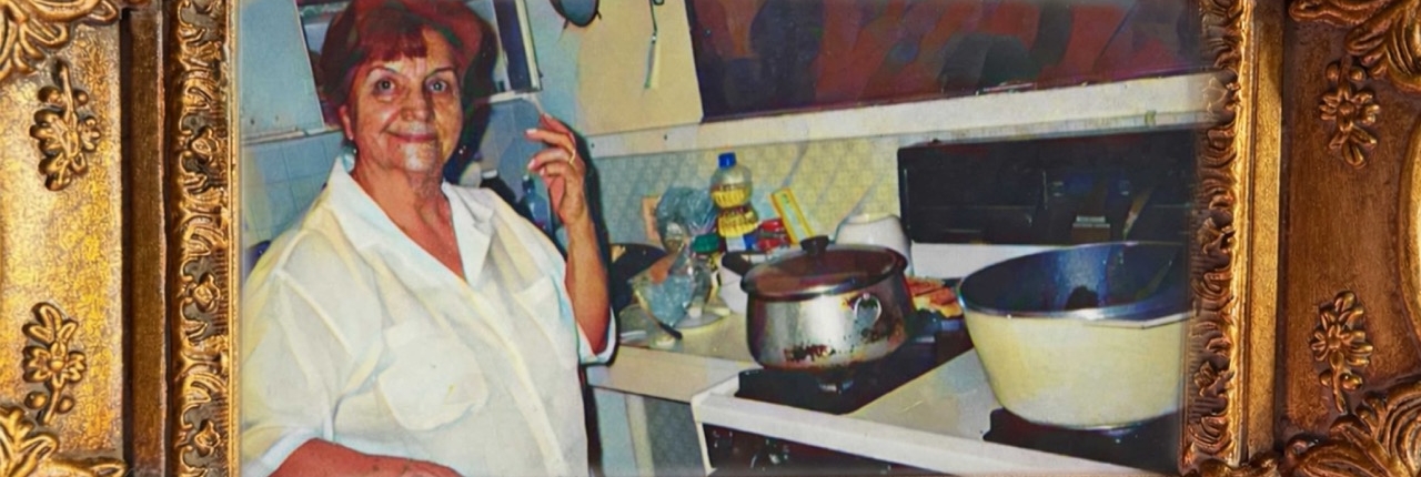 A framed vintage photograph of an older woman smiling in her kitchen, with pots on the stove. A gold banner reads "Abuelita's Kitchen is home."
